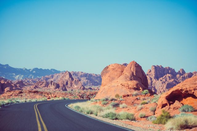 Curving road cutting through a barren desert landscape with striking red rock formations. Ideal for travel blogs, adventure promotions, scenic drives, outdoor activities, and tourism websites.