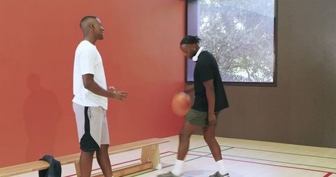 Passing and dribbling basketball: two african american men laughing on indoor court