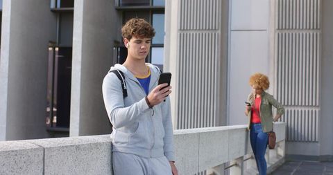 Diverse people leaning on concrete railing checking phones with earbuds and backpack