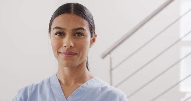 Image of happy biracial female doctor standing at stairs, looking at camera. Health, medicine and prevention concept.