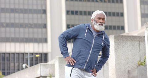 Senior african american man pausing during outdoor workout in urban plaza wearing hoodie