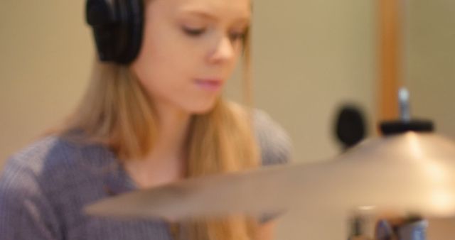 Focused caucasian female musician wearing headphones and playing drums in studio room. Music, technology and lifestyle, unaltered.