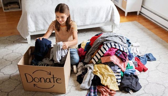 Preteen girl sorting and packing clothes for charity donation in bright cozy home bedroom