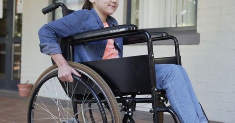 Adolescent female sitting in manual wheelchair on porch pushing rim showing mobility independence