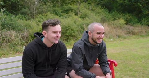 Two men relaxing on bench in park enjoying conversation