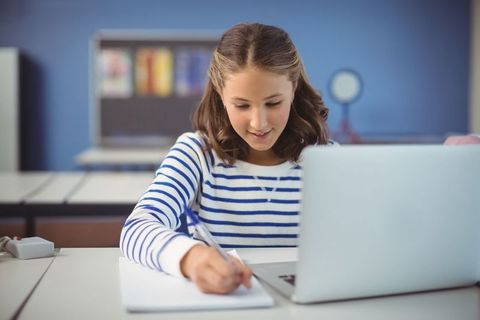 Focused student taking notes in classroom with laptop