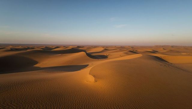 Glowing sunrise lighting rippled desert dunes with curved ridges and deep shadows