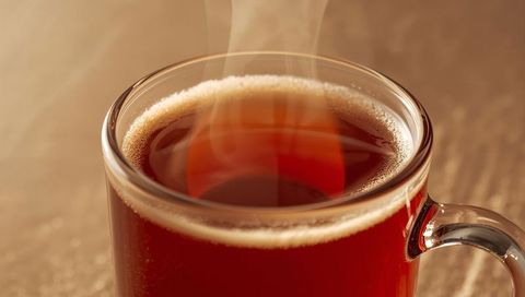 Steaming Clear Glass Mug with Amber Tea Resting on Wooden Tabletop and Foam Ring