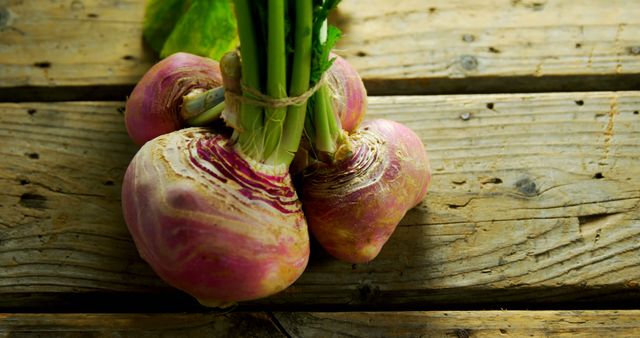 Freshly harvested turnips with stems lying on rustic wooden surface. Turnips show natural organic texture and earthy colors, highlighting their farm fresh appeal. Suitable for use in articles about organic farming, fresh produce, gardening, healthy eating, and root vegetables.