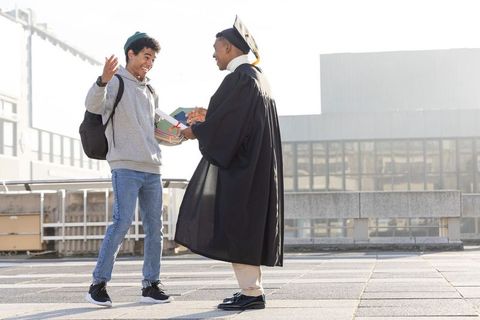 Graduate receiving diploma on urban rooftop while friend celebrating together