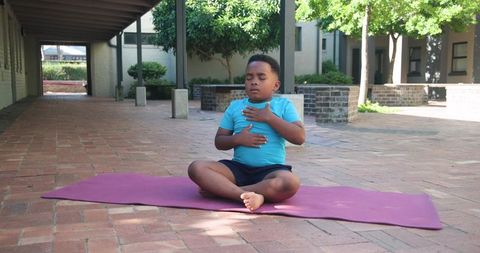 African american boy meditating on purple yoga mat in brick courtyard practicing breathing