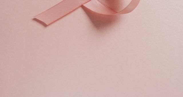 Elegant pink ribbon lying on a pastel pink background. Perfect for breast cancer awareness campaigns, feminine design projects, or any material related to support and awareness initiatives. The soft texture and muted tones make it suitable for invitations, greeting cards, or background elements.