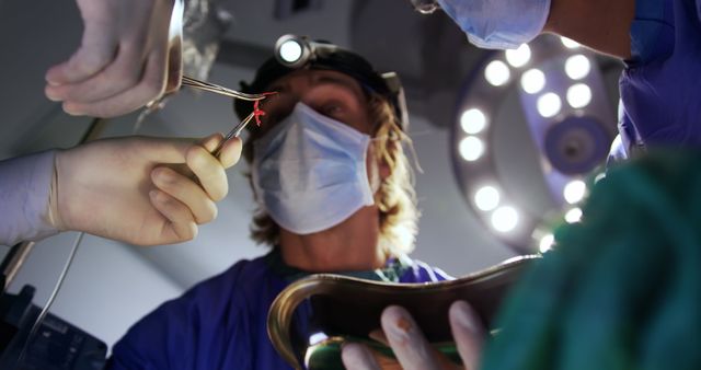 Medical team in a brightly lit operating room performing surgical procedure with precision. Surgeons wearing masks and gloves using surgical instruments. Ideal for content on healthcare, medical practice, hospitals, and surgical procedures.