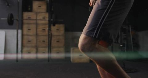 Male athlete lunging wearing red knee support in gym with plyo boxes and squat rack