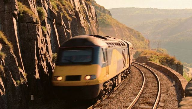 High-speed yellow-gray locomotive rounding cliffside curves on coastal railway at dusk