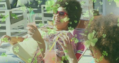 Friends sipping pink cocktails while relaxing on sunlit deck with clover overlay