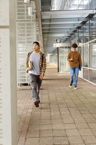 Diverse male students walking modern campus walkway carrying notebooks and apple