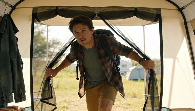 Male camper pulling tent mesh flaps stepping out with backpack at sunny campsite morning