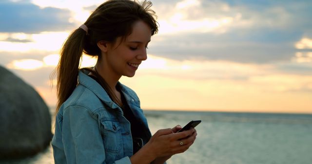 Smiling Young Woman Texting on Smartphone at Seaside During Sunset - Download Free Stock Images Pikwizard.com