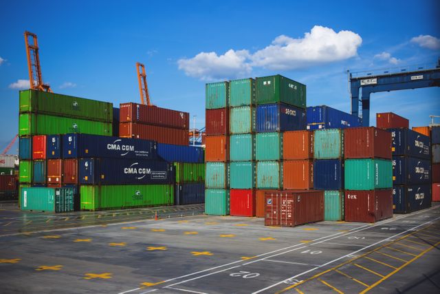 Image depicts stacked cargo containers at a shipping port with a bright, clear sky. Ideal for articles and visuals related to international shipping, logistics, global trade, industrial processes, freight transportation, and commercial port activities.
