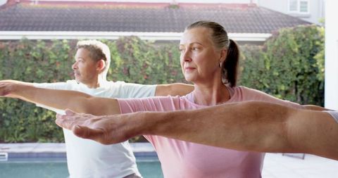 Adults practicing yoga outdoors poolside in sunlight