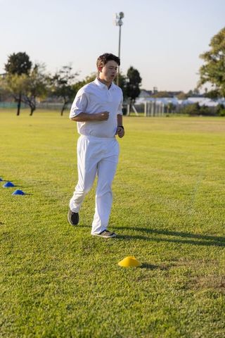 Young athlete running training drill on grass outdoors with markers and wristwatch