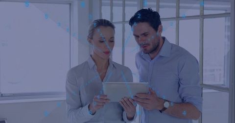 Two Professionals Reviewing Tablet Data with Blue Digital Overlay in Modern Office