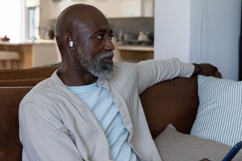 Mature african american man relaxing on leather sofa listening with wireless earbuds