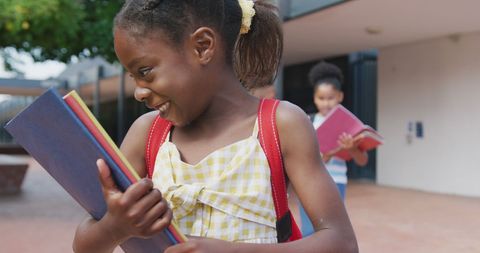 Joyful African American girl embracing stacked books outdoors