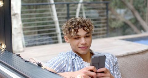 Young Man Relaxing with Smartphone Outdoors under String Lights