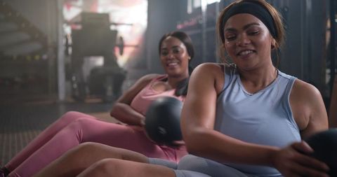 Diverse women performing medicine ball twists in gym for core strength and motivation
