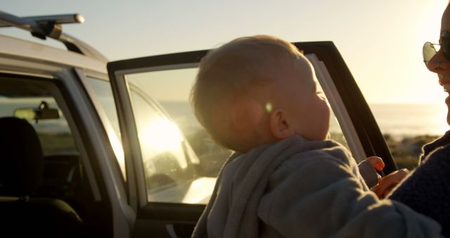 Mother holding baby outdoors by car during sunset - Download Free Stock Images Pikwizard.com