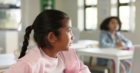 African american schoolgirl gazing attentively in classroom with blurred classmate behind