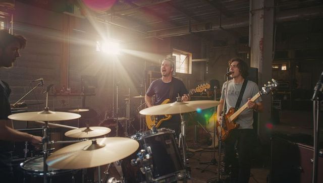 Garage rock trio practicing with drums, bass and electric guitar under sunbeam lensflare