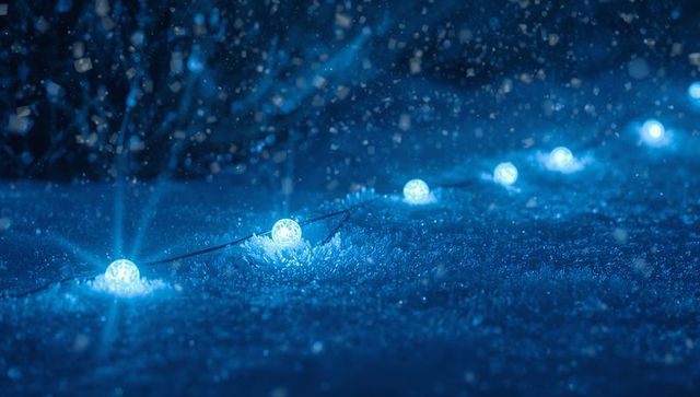 Glowing blue spherical led string lights casting soft halos on snow at night frosty bokeh