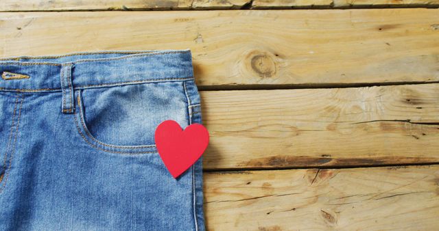 Close up of jeans with red heart on wooden background with copy space. Denim day, material, style and design concept.