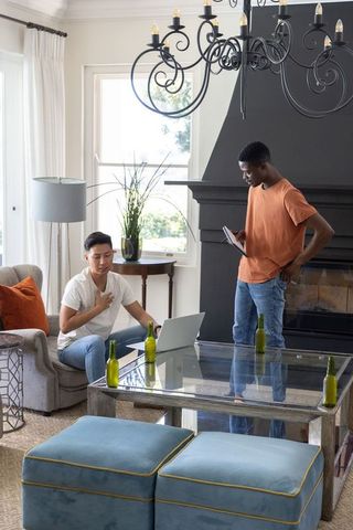 Diverse friends collaborating remotely in bright living room using laptop and tablet