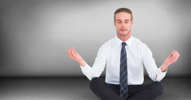 A businessman in a white shirt and dark tie sitting cross-legged in a gray room, practicing meditation. This image represents stress relief, corporate wellness, mindfulness, and relaxation. Perfect for use in articles, blogs, and promotions related to workplace wellness programs, stress management techniques, and the importance of taking breaks during busy work schedules.