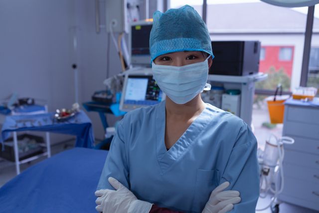 Female surgeon in operation room wearing a surgical mask and scrubs with arms crossed, exuding confidence and professionalism. Ideal for illustrating themes of healthcare, medical professionals, surgery, and hospital environment.