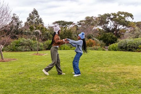 Teenage african american friends spinning and laughing on lawn wearing beanies