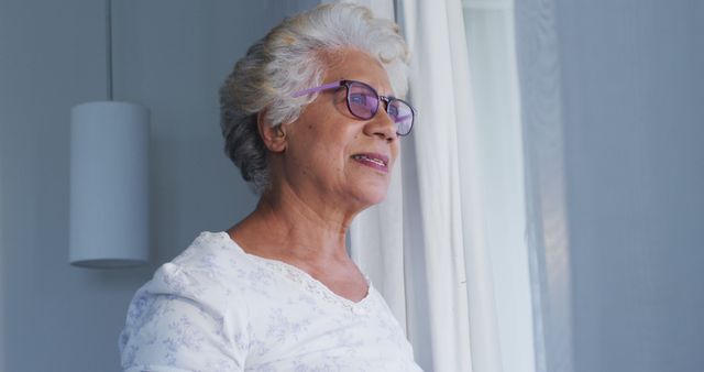 Thoughtful african american senior woman with hand on chin looking out of the window at home. retirement senior lifestyle living in quarantine lockdown concept