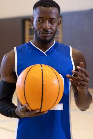 Focused african american basketball player holding ball wearing blue jersey indoor court