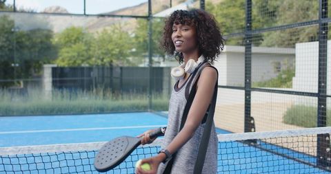 African woman playing pickleball on blue outdoor court with paddle and ball
