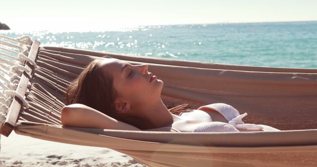 Young woman enjoying a peaceful moment on a hammock by the beach. Perfect for travel, vacation, and lifestyle publicity. Use for articles about relaxation, beach holidays, or summer fun.