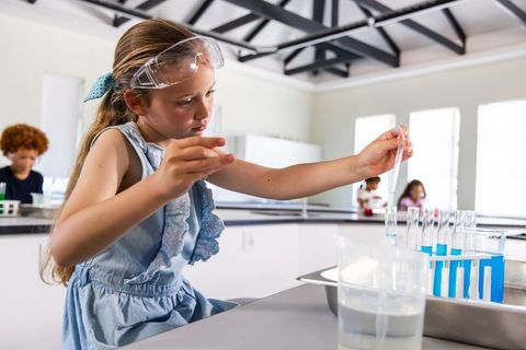 Young girl conducting hands-on chemistry experiment with test tubes and safety goggles