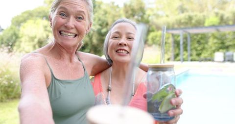 Joyful senior women celebrating by the poolside with refreshing drinks