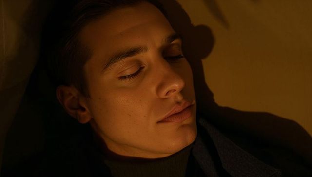 Moody closeup of young man resting with eyes closed, warm shadowed cinematic intimate portrait