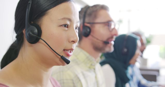 Asian woman and Caucasian man work in a busy call center office. They're wearing headsets, focused on providing customer support.