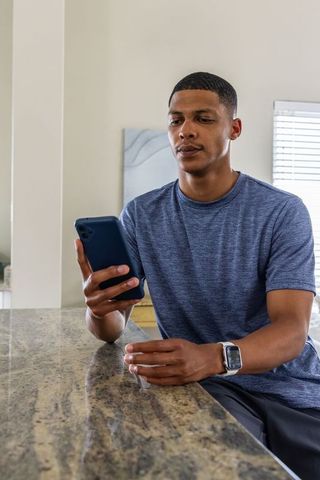 African american man checking smartphone at granite kitchen island wearing smartwatch