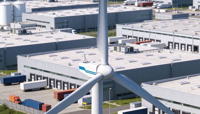 Wind turbine above logistics park rotating nacelle with warehouses, containers, trailers